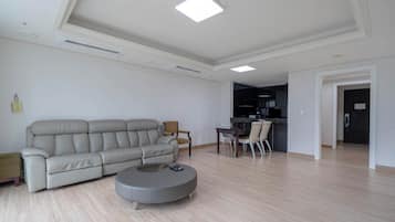 A modern living room with a sofa, a round coffee table, and a dining area with chairs.