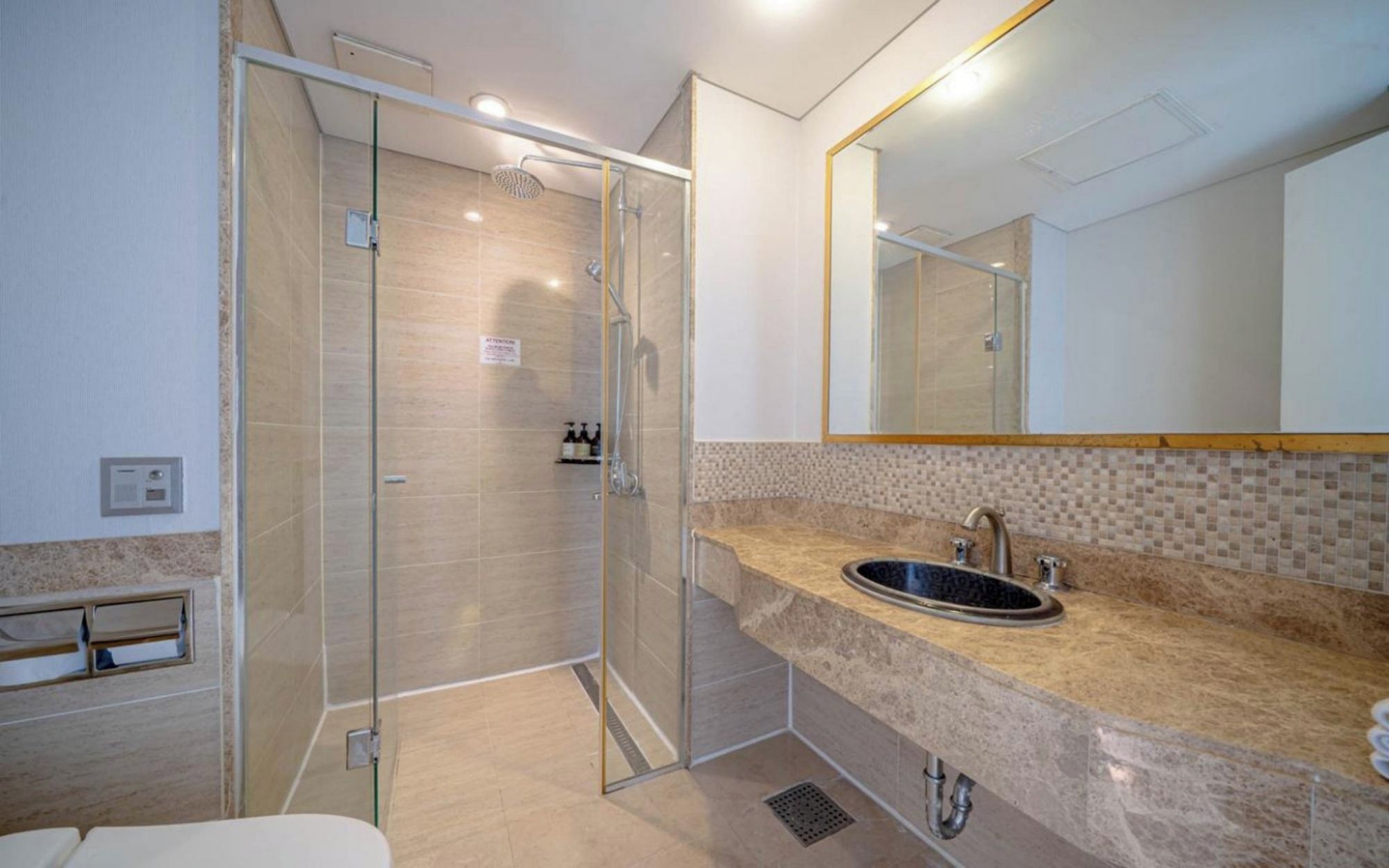 A modern bathroom with a glass shower enclosure, a sink with a marble countertop, and a large mirror.
