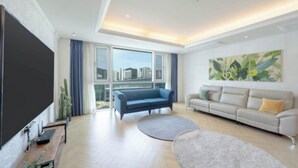 A modern living room with a large flat-screen TV, two sofas, a large window with a city view, and a painting on the wall. - BS centum hotel (Busan)