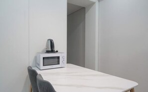 A white microwave on a white table in a room with white walls. - BS centum hotel (Busan)