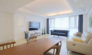 A modern living room with a wooden dining table, a sofa, and a TV mounted on the wall. - BS centum hotel (Busan)
