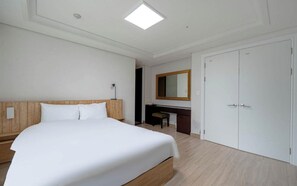 A hotel room with a large bed, a desk, a mirror, and a wardrobe.