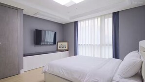 Une chambre à coucher moderne, avec un lit, un téléviseur à écran plat, un tableau encadré et une fenêtre avec des rideaux.