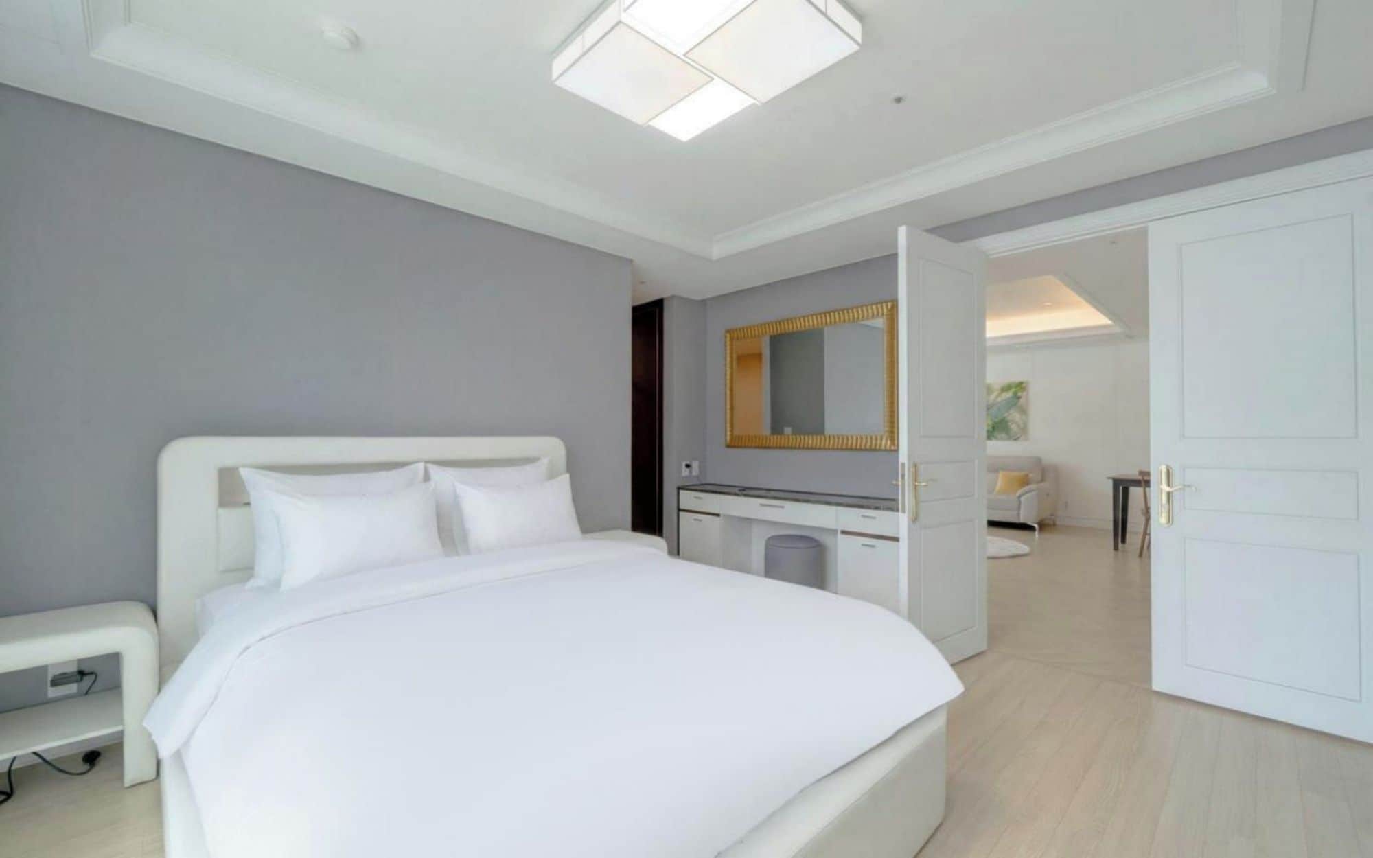 A modern hotel room with a large bed, a desk, a mirror, and a wardrobe.