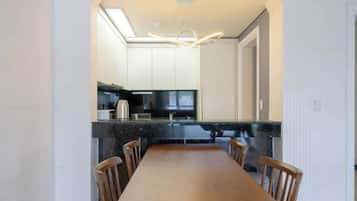 A modern kitchen with a long dining table and chairs, a built-in oven, and a large window.