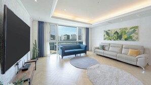 A modern living room with a large flat-screen TV, two sofas, a coffee table, and a large window with a city view. - BS centum hotel (Busan)