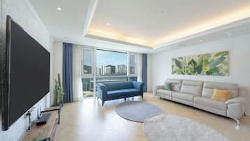 A modern living room with a large flat-screen TV, two sofas, a coffee table, and a large window with a city view.