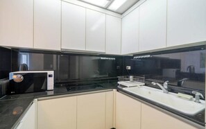 A modern kitchen with white cabinets, a black countertop, a microwave, and a sink.