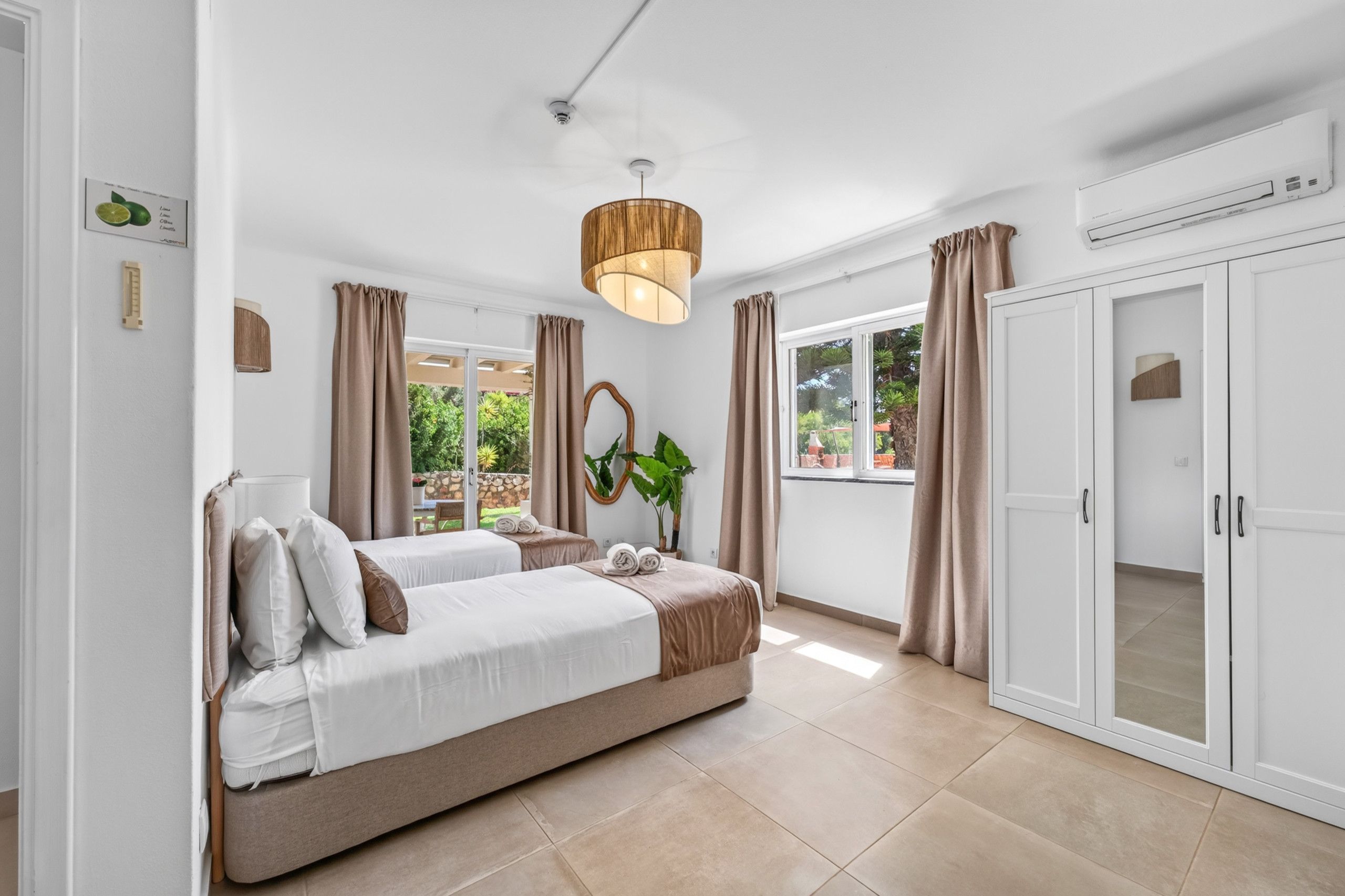 A bedroom with two beds, a large window, a ceiling fan, and a wardrobe.