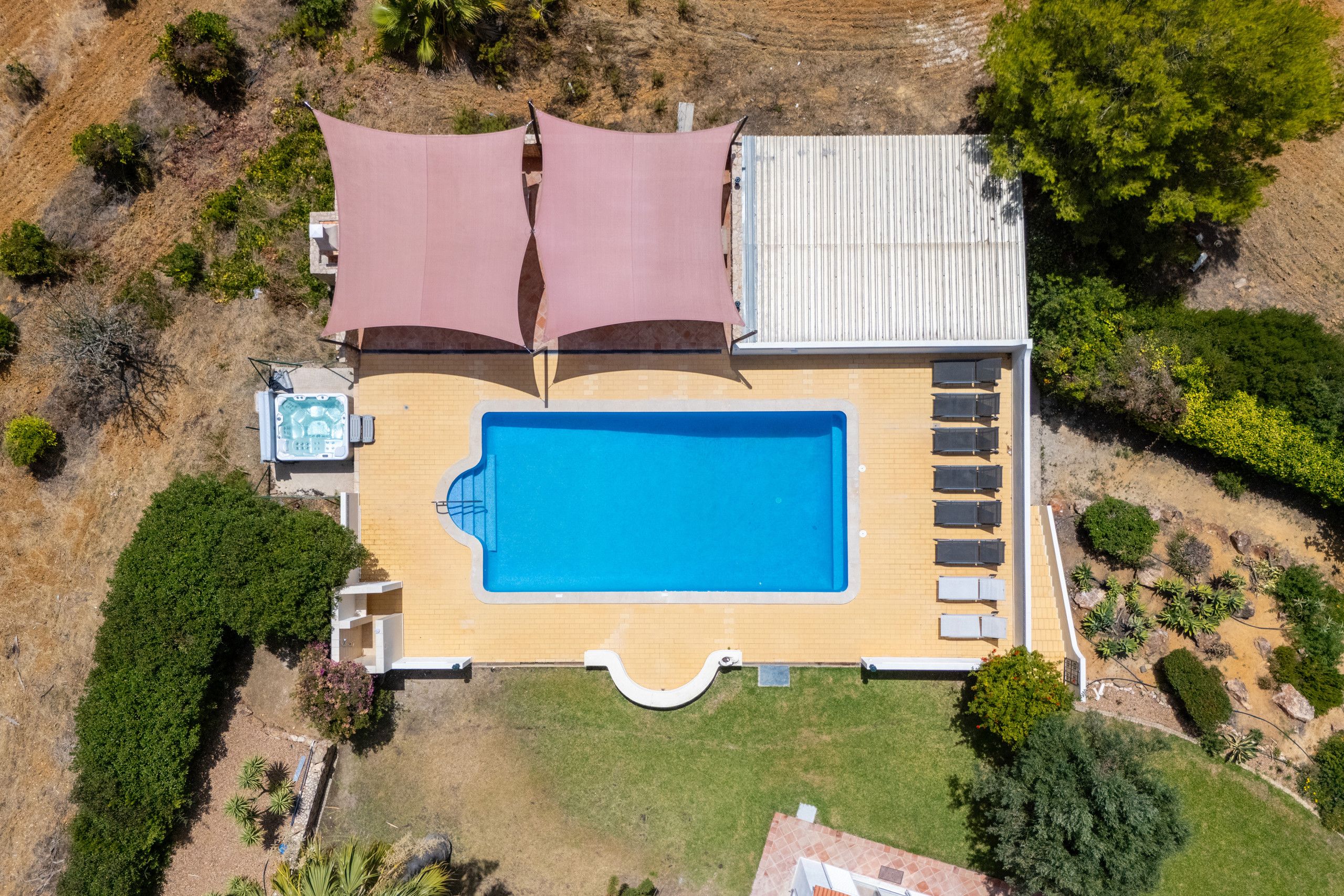 An aerial view of a residential property with a swimming pool, a hot tub, and a covered patio area.