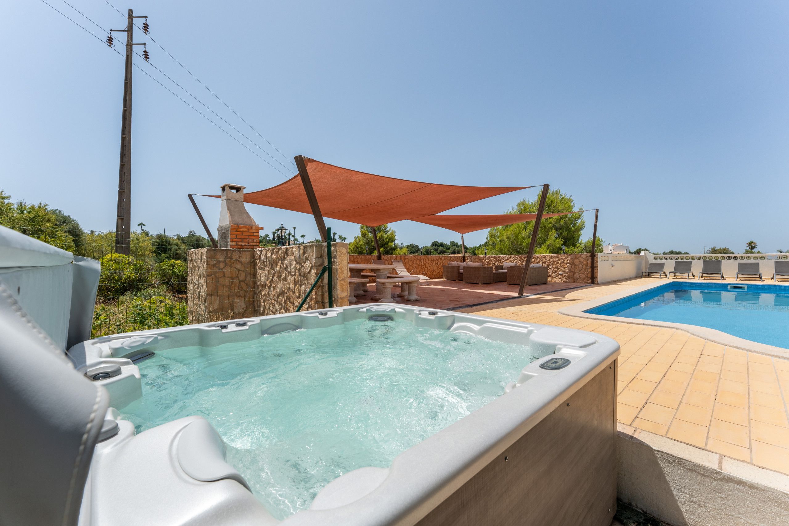 Un jacuzzi y una piscina con sillas de descanso y un muro de piedra.