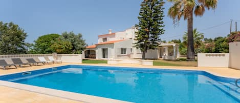 Una piscina con borde de azulejos, rodeada por una terraza pavimentada. Hay sillas de descanso a lo largo de la piscina.