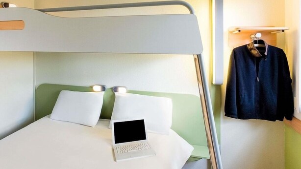A bunk bed with a laptop on the lower bunk, a hanging coat rack, and a bedside table with a lamp. - Ibis Budget Dijon Saint Apollinaire (Saint-Apollinaire)