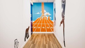 A hallway with a blue wall featuring a large mural of a runner on a track, a wooden floor, and a white ceiling. - Ibis Budget Dijon Saint Apollinaire (Saint-Apollinaire)