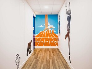 Ein Flur mit blauer Wand, die ein großes Wandbild eines Läufers auf einer Bahn zeigt, Holzboden und weißer Decke.