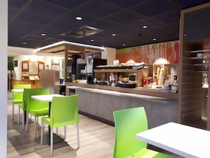A restaurant with a counter, green chairs, and a menu board. - Ibis Budget Dijon Saint Apollinaire (Saint-Apollinaire)