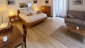 Une chambre à coucher avec un lit, des tables de chevet, un bureau, une chaise, un canapé et une fenêtre.