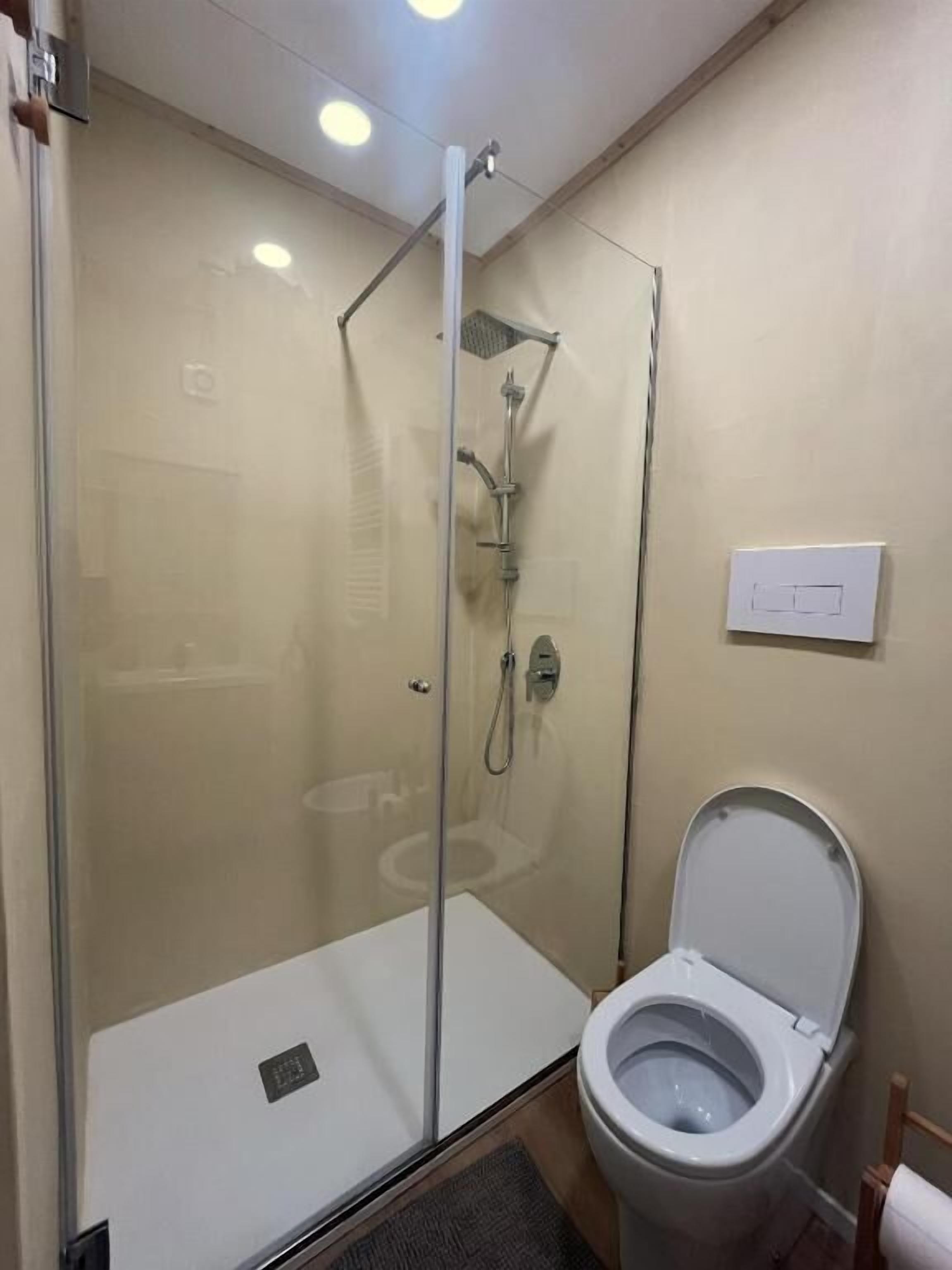 Une salle de bain avec une douche à parois de verre, des toilettes et un interrupteur fixé au mur.