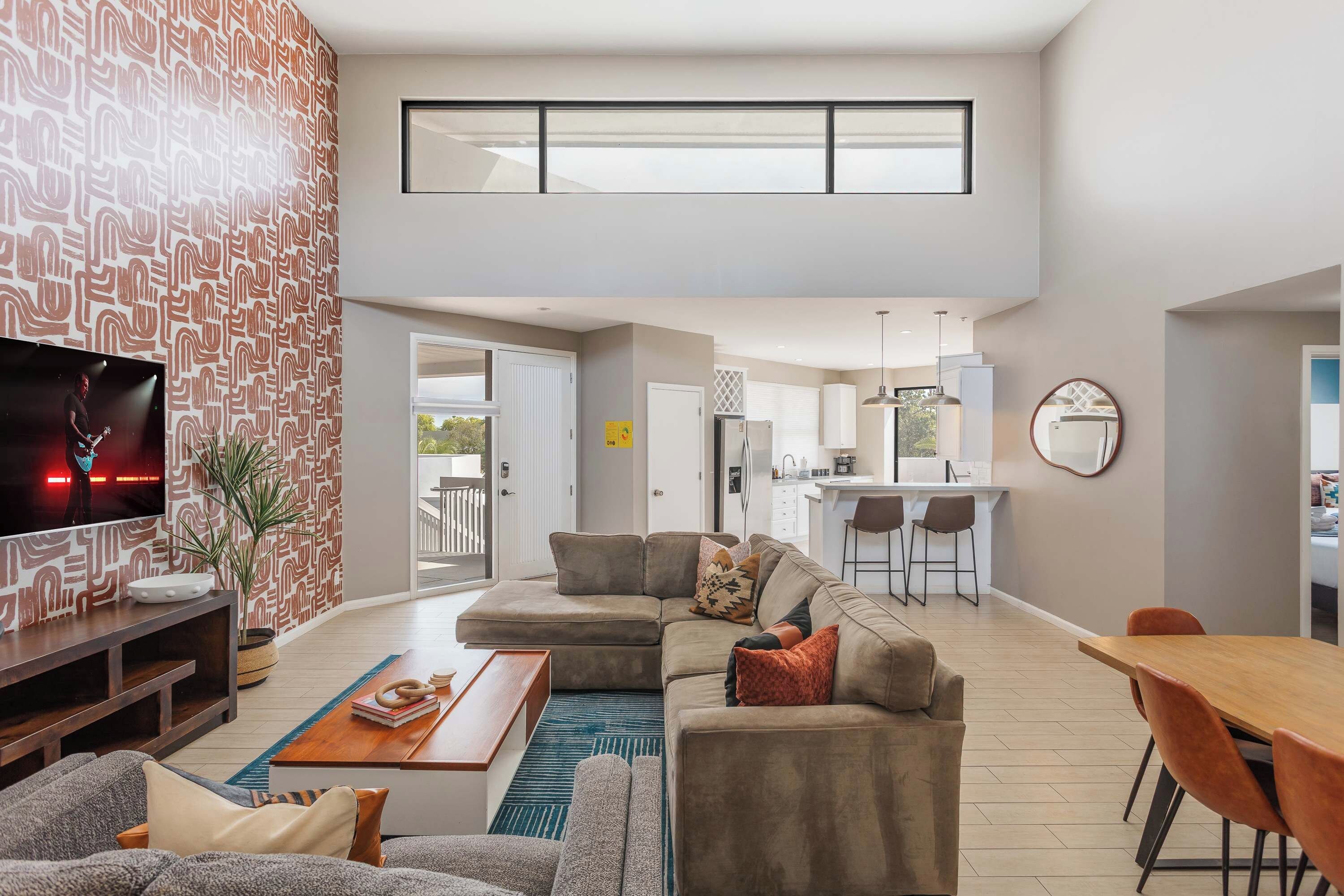 A modern living room with a sectional sofa, a coffee table, and a TV on a wall with a patterned wallpaper.