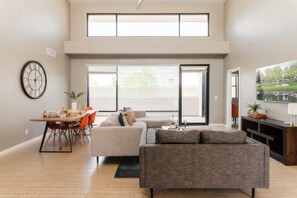 Ein modernes Wohnzimmer mit einer Couch, einem Esstisch und einem großen Fenster.