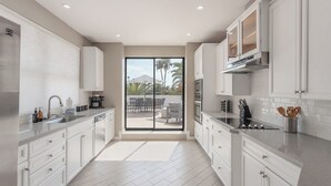 Une cuisine moderne avec des meubles blancs, un évier en acier inoxydable et une grande porte-fenêtre coulissante donnant sur une terrasse extérieure.