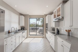 A modern kitchen with white cabinetry, a stainless steel sink, and a large sliding glass door leading to an outdoor patio. - Vega - Private Balcony - In Old Town Scottsdale (Scottsdale)