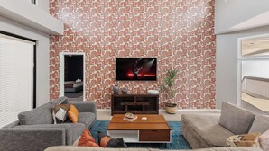 Un salon moderne avec un papier peint à motifs, un téléviseur à écran plat et un coin salon confortable agrémenté d’une table basse.