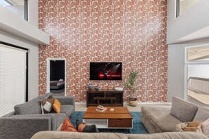 A modern living room with a patterned wallpaper, a flat-screen TV, and a comfortable seating area with a coffee table. - Vega - Private Balcony - In Old Town Scottsdale (Scottsdale)