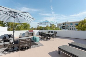 Eine Außenpatio mit Grill, Sitzgelegenheiten und Sonnenschirmen.