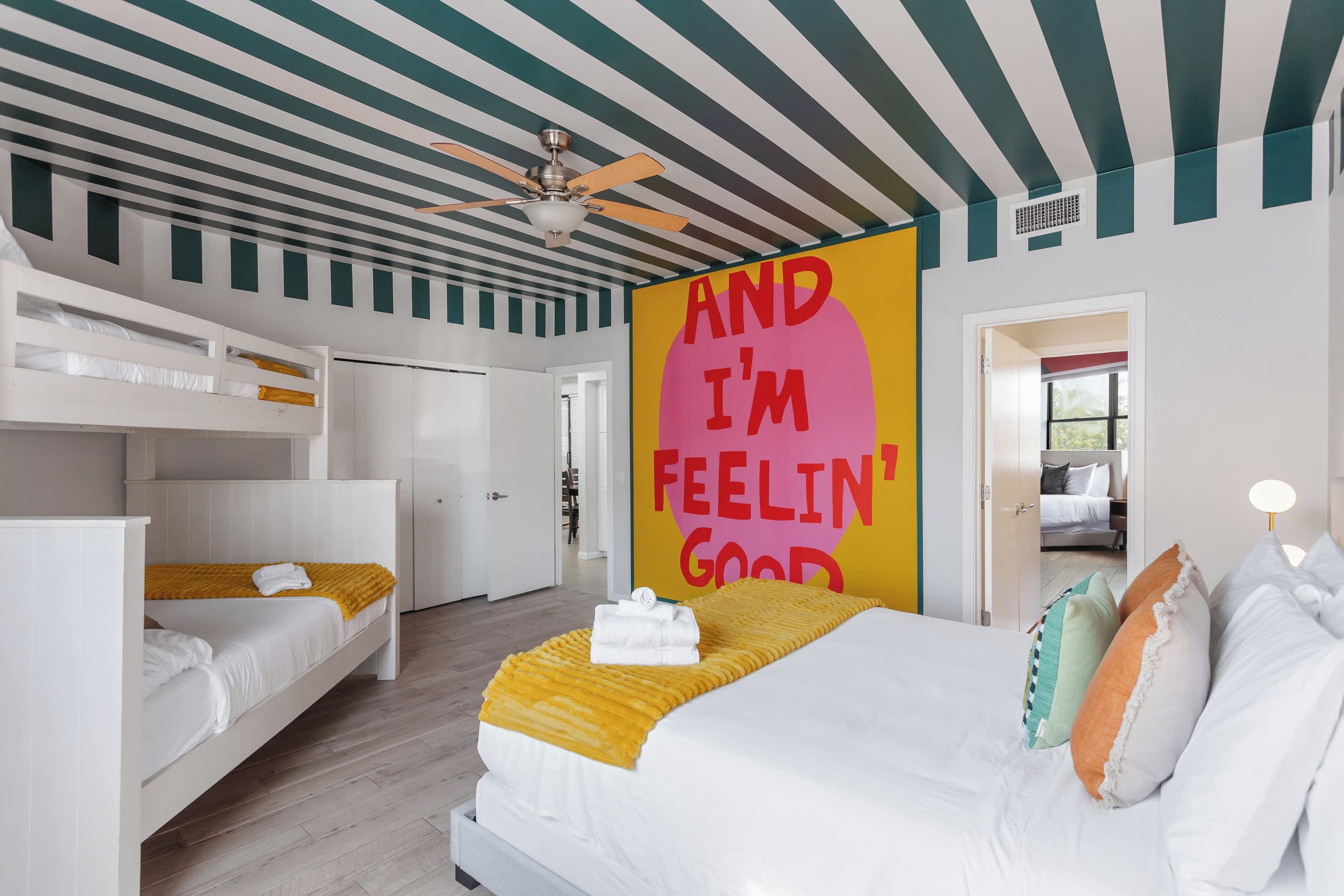 A hotel room with a bunk bed, a single bed, a ceiling fan, and a motivational poster.