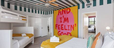 A hotel room with a bunk bed, a single bed, a ceiling fan, and a motivational poster.