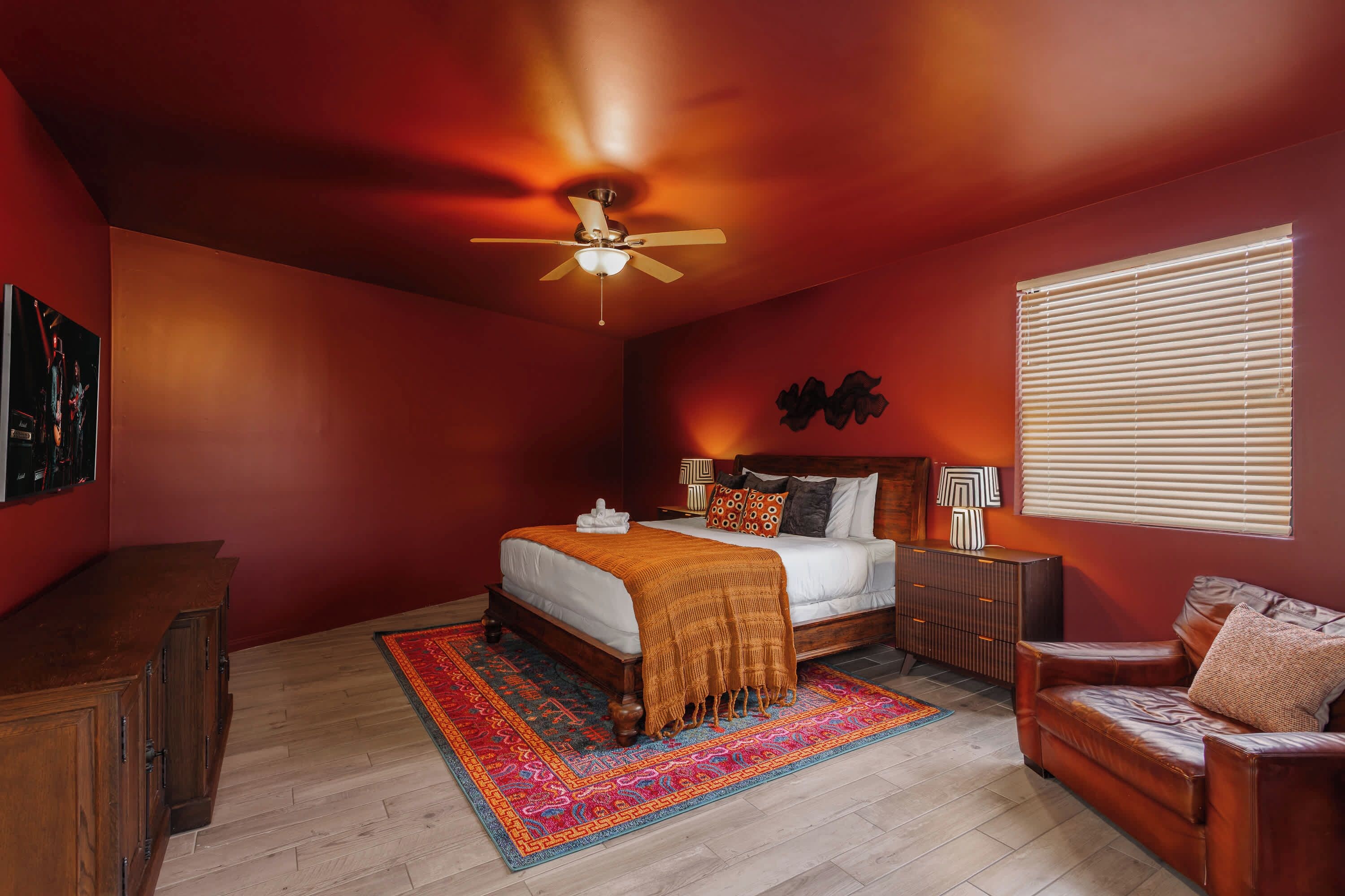 A bedroom with a bed, a nightstand, a chair, a window with blinds, and a ceiling fan.