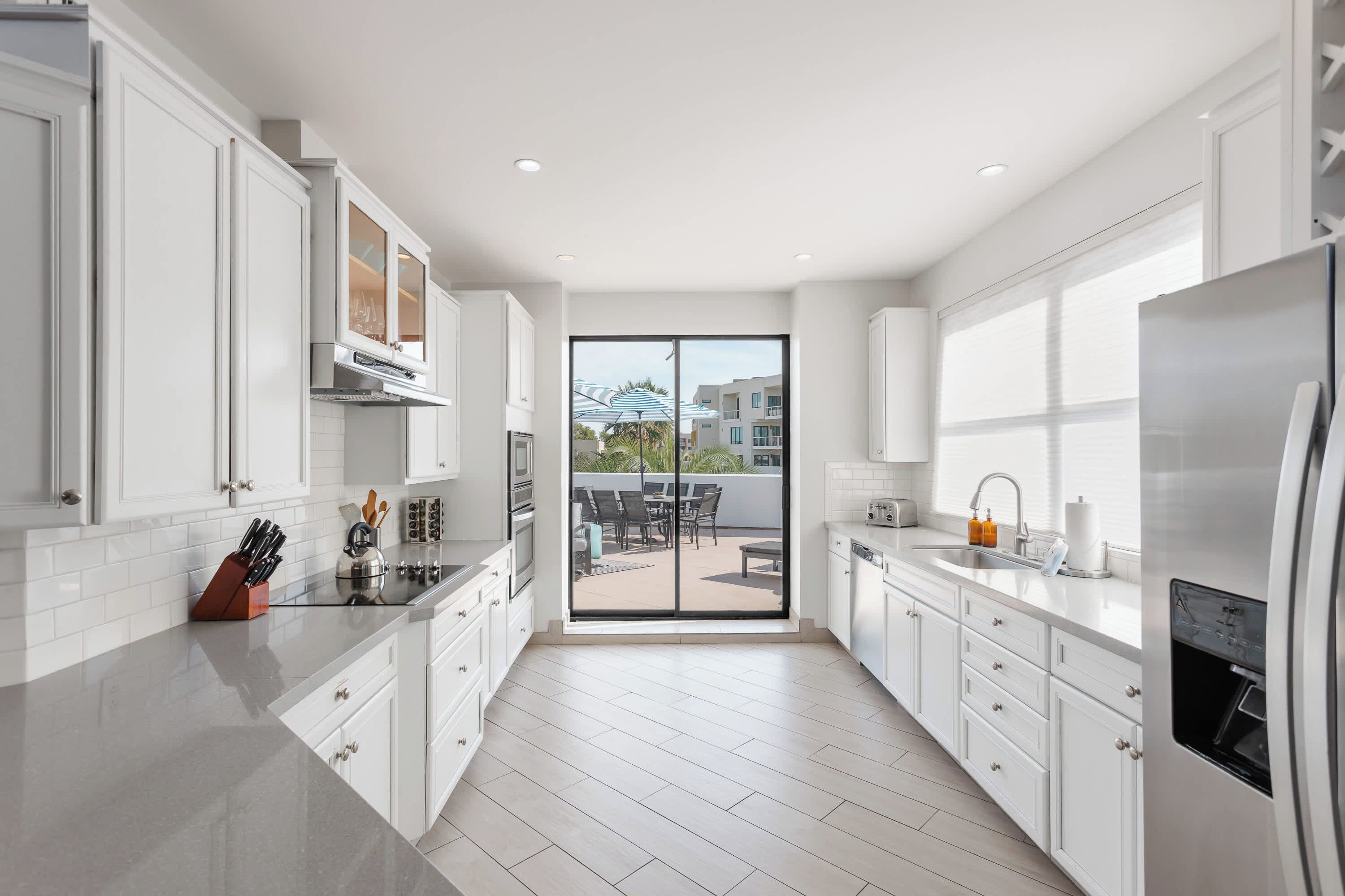 A modern kitchen with white cabinetry, a stainless steel refrigerator, and a view to an outdoor patio area.