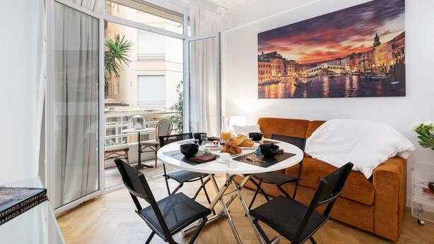 Ein modernes Wohnzimmer mit Essbereich, einer Couch und einem großen Fenster mit Blick auf Gebäude.