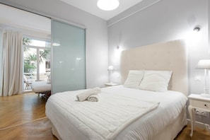 A hotel room with a large bed, a nightstand, a lamp, and a sliding glass door leading to a balcony. - Promenade Flat for 3 Guests | 30+ Night Stay (Nice)