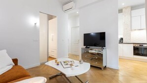 Ein modernes Wohnzimmer mit Sofa, Couchtisch, Flachbildfernseher und einer Küche im Hintergrund.