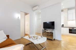 A modern living room with a sofa, a coffee table, a flat-screen TV, and a kitchen area in the background. - Promenade Flat for 3 Guests | 30+ Night Stay (Nice)