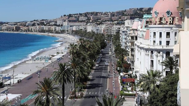 A coastal cityscape with a beach, palm-lined promenade, and historic buildings. - Large 3-Room Garibaldi – 4 People | Stay 30+ Days (Nice)