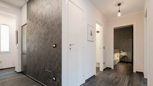 A hallway with a modern design, featuring a textured wall, a white door, and a dark wooden floor. - Large 3-Room Garibaldi – 4 People | Stay 30+ Days (Nice)