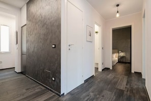 Ein Flur mit modernem Design, der sich durch eine strukturierte Wand, eine weiße Tür und einen dunklen Holzboden auszeichnet.