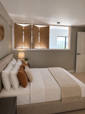 Ein Schlafzimmer mit einem großen Bett, einem Nachttisch mit Lampe, einem Fenster mit Ausblick und einem Kleiderschrank.