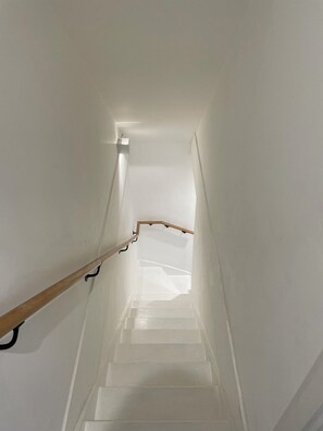 Eine schmale Treppe mit weißen Wänden und einem hölzernen Geländer.