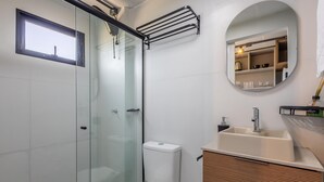 A modern bathroom with a glass shower enclosure, a white toilet, a sink with a mirror above it, and a towel rack. - Loft 50 m From Camacho Beach Plo0005 (Jaguaruna)