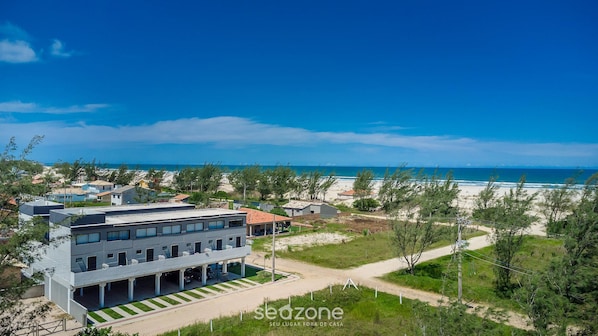 A modern building with a flat roof, a covered parking area, and a view of the beach. - Loft 50 m From Camacho Beach Plo0005 (Jaguaruna)