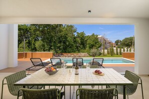 A dining area with a table and chairs, a pool in the background, and a view of trees and buildings. - Villa Astrid (Istria - Krničari) (Krničari)