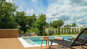 Une terrasse en bois avec une piscine, des chaises longues et une table garnie de fruits.