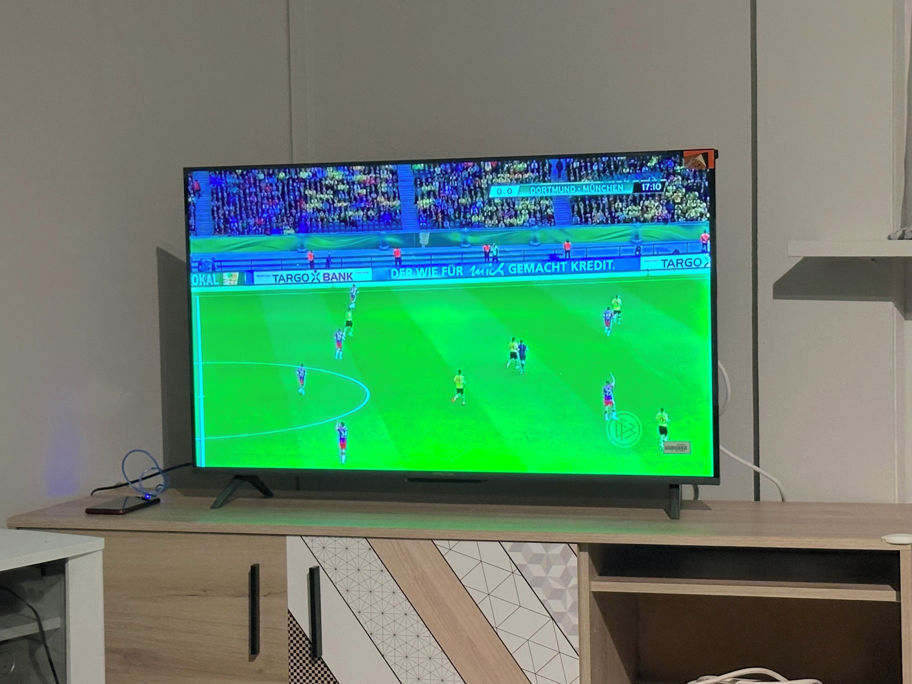 Un televisor mostrando un partido de fútbol con un marcador de 0-0 y el tiempo indicado en 17:10.