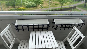 A balcony with a white table and two chairs, a metal railing, and a view of a garden. - Helsinki Airport & City Center Gateway (Helsinki)