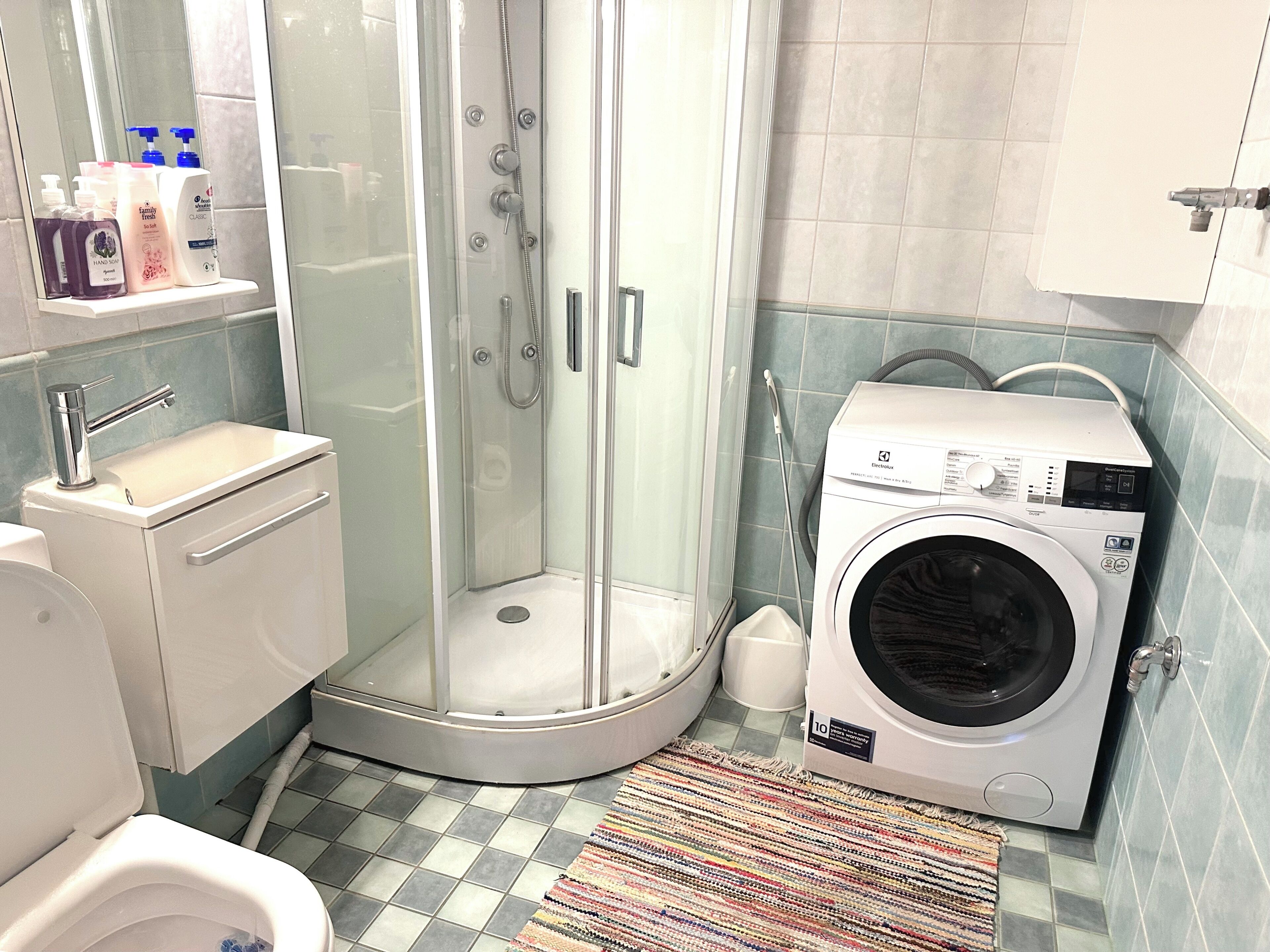 A bathroom with a glass-enclosed shower, a washing machine, a sink, and a toilet.