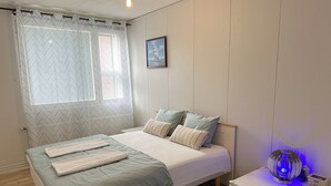 A bedroom with a bed, a bedside table with a lamp, a window with curtains, and a picture on the wall. - Helsinki Airport & City Center Gateway (Helsinki)